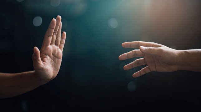 Conceptual image of two hands interacting in dark space, one hand reaching out for help or connection while the other hand pushes away in refusal or rejection gesture