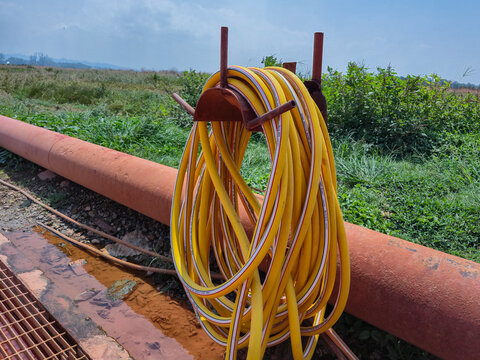 Yellow high pressure water hose coiled on stand at outdoor industrial and agricultural irrigation site with pipeline background