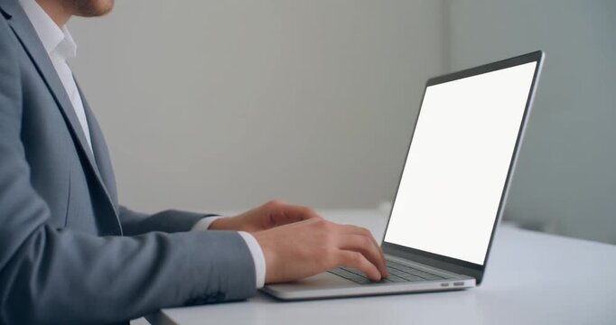 Executive man in gray suit typing on laptop with empty white display