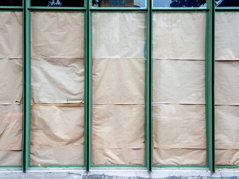 Storefront windows covered from the inside with brown kraft paper. Green metal frames surround the large glass panels. Ideal for concepts like business closure, renovation, or coming soon.