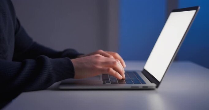 Man typing on notebook keyboard with empty glowing screen at night