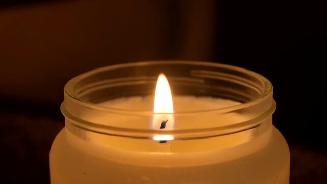 Close up of a lit candle in a glass jar with a dark background.