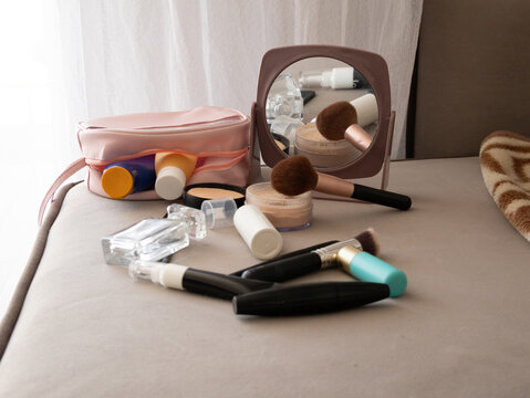 Pink cosmetic bag with makeup items and round mirror on cluttered vanity