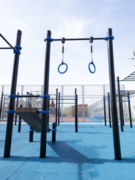 Outdoor gym rings and parallel bars in public park under blue sky, inviting training