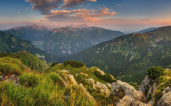 Breathtaking evening view of Tatra National Park in Slovakia. Majestic mountain ridges and deep valleys stretch under beautiful warm orange clouds during a dramatic summer alpine sunset.