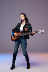 Fototapeta premium Confident young woman holding electric bass guitar in studio
