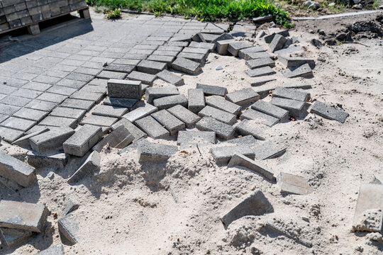 Driveway paving brick removal and sandy subgrade preparation showing displaced concrete setts and interlocking pavers on a construction site