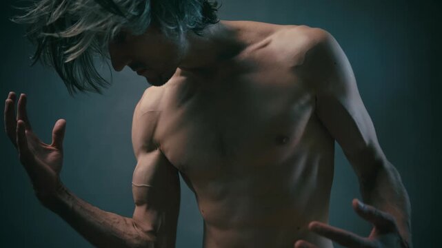 awareness of one's power Shirtless middle-aged gray-haired man posing dynamically with raised arms in studio under dramatic low-key lighting, highlighting muscular definition