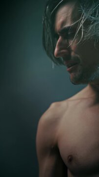 suffering bitterness pain Side-profile portrait of a shirtless young man with long hair in dramatic studio lighting, highlighting defined facial and body contours against a dark background