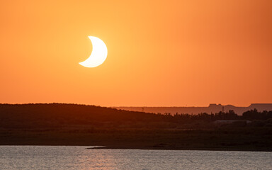 Telephoto view of crescent eclipsed sun setting over San Salvador reservoir, Spain. © PABLO