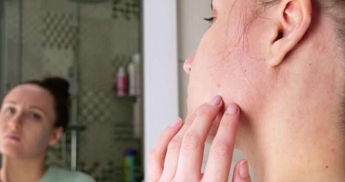 Woman carefully examines her facial skin in bathroom mirror. Close-up highlights skin texture, daily skincare routine, healthy complexion and personal commitment to maintaining naturally beautiful ski