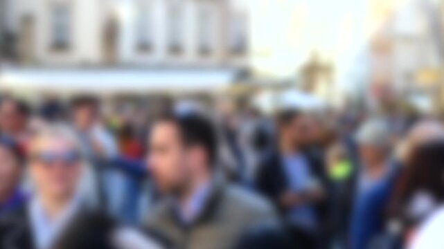 Large crowd of anonymous, unrecognizable people walking on a busy city street. The scene is intentionally blurred, creating a bokeh effect and focusing on the concept of society and urban life