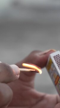 Close-up of hands striking a match against a matchbox, producing a bright flame