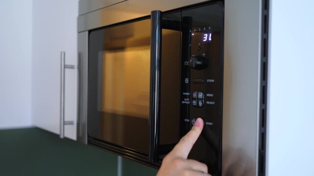 Female hand opening a modern microwave oven, placing a lunch box with a pre cooked meal inside, closing the door, and setting the timer to reheat the food in a contemporary kitchen