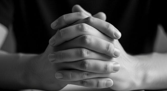 Close-up monochrome photograph of intertwined human hands in a gesture of prayer or contemplation