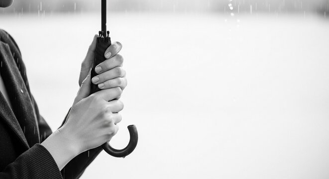 Close-up monochrome portrait of hands holding an umbrella handle during rain