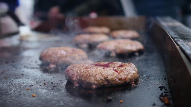 Delicious beef burger patties cooking on a hot, oiled griddle, sizzling and releasing flavorful steam. A perfect depiction of classic american street food preparation at a barbecue or festival