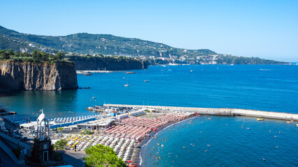 Naklejka premium Aerial photograph capturing the crowded Alimuri beach in Meta, Sorrento Peninsula, Italy, on a vibrant mid-August summer day. Features turquoise water, sun umbrellas, coastal road, and background clif