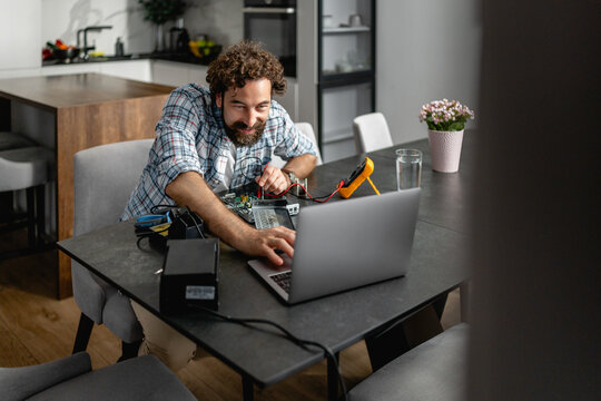 Man repairing laptop with multimeter at dining table while troubleshooting electronics and working remotely