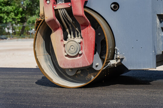 Industrial heavy machinery asphalt compactor drum operating on freshly paved roadway surface during commercial roadworks and civil development