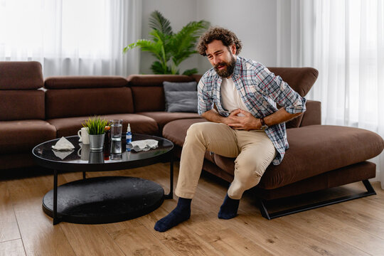 Man clutching stomach in pain while sitting on living room couch at home