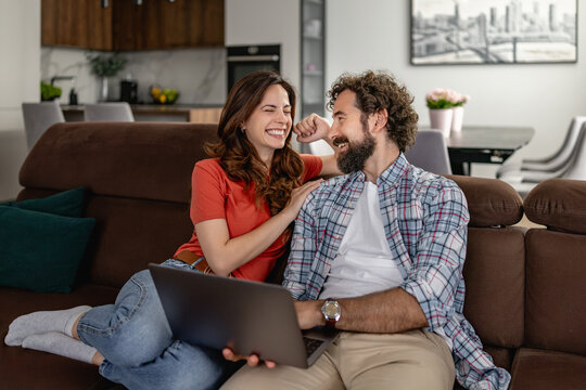 Smiling couple relaxing on sofa with laptop sharing a laugh in modern living room