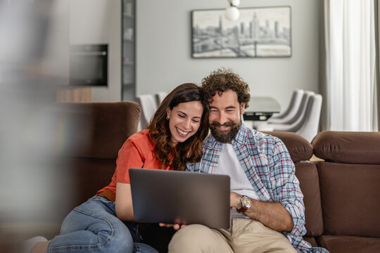 Couple on couch using laptop at home smiling and enjoying a cozy moment together