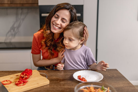 Mother and daughter cooking together in kitchen preparing peppers and salad, sharing a tender moment