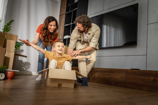 Happy family playing and unpacking while moving into new home with child in cardboard box