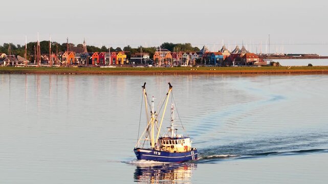 Fishing trawler sailing on calm water with colorful village background
