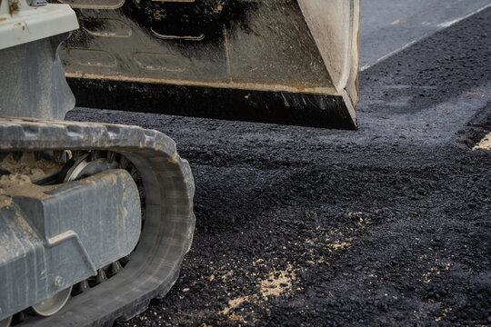 Compact excavator track and grading bucket spreading fresh hot asphalt pavement during road construction and civil infrastructure development