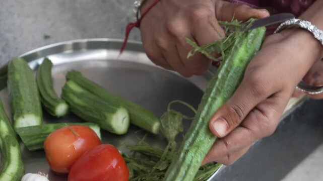 Person peeling and cutting fresh ridge gourd with tomatoes on a steel tray