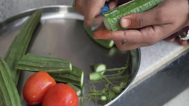Person peeling and cutting fresh ridge gourd (tori) with tomatoes on a steel tray