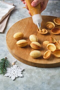Step-by-step preparation of shortbread cookies in the shape of a nut with a filling of boiled condensed milk on a gray concrete background.