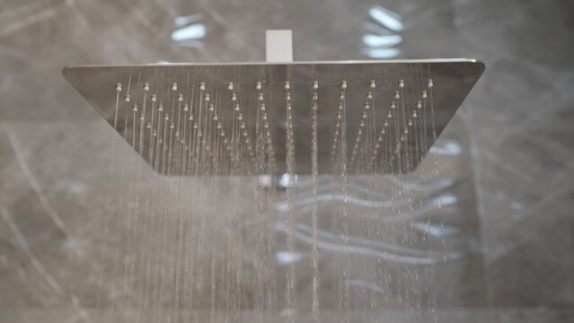 Modern square rain shower head with water streams against marble tile