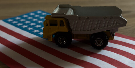 nostalgic toy dump truck stationary on an american flag in side view with plastic and metal materials and yellow and gray colors, evoking a sense of patriotism and childhood memories. © Angelov