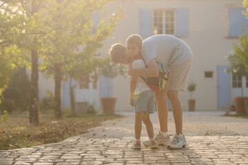 Fototapeta premium Father and son hugging, in outdoor cobblestone path residential area, with trees, house with blue shutters, cobblestone path, from a eye-level perspective perspective.