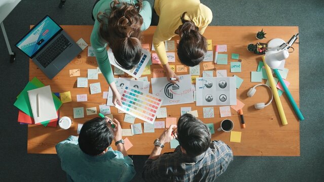Top view of business team write graphic logo on meeting table with colorful sticky notes and design while explain idea. Project manager sharing idea and explain concept art to smart team. Symposium.