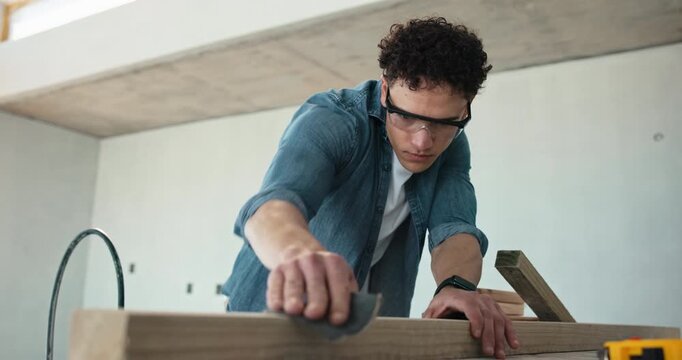 Carpenter, man and sanding in construction site with wood, building furniture or restoration project. Person, sandpaper and blow dust with smooth timber, craftsmanship skills and carpentry career.