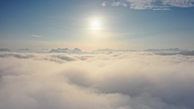 Sun rising above thick blanket of clouds, distant limestone mountains peaking through the mist in KHAO SOK National Park, Thailand. Expansive aerial view of morning sunrise sky. Drone flight footage