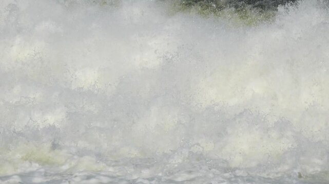 High angle slow motion view of massive white water foam tumbling down a dam spillway with a small swallow bird flying across the frame.
