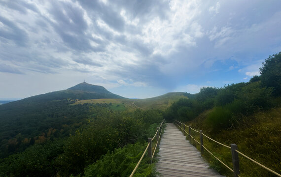 wooden boardwalk leading into a hilly terrain with lush vegetation and distant mountains, peaceful and serene outdoor recreation setting with rope railings and natural greenery.