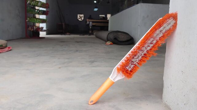 Orange feather duster in warehouse. Cleaning equipment close up. Static shot of industrial interior hygiene tool