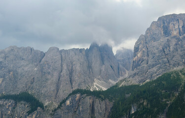 Naklejka premium mystical and serene mountain range with cloud-covered peaks in an alpine landscape viewed from an aerial perspective featuring rocky cliffs and evergreen trees.