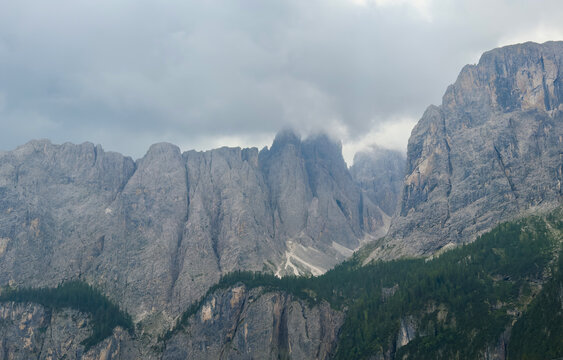 mystical and serene mountain range with cloud-covered peaks in an alpine landscape viewed from an aerial perspective featuring rocky cliffs and evergreen trees.