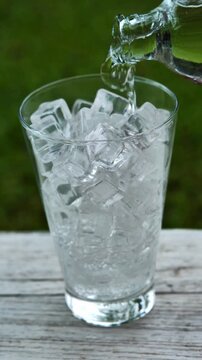 Pouring soda into an ice-filled glass in a bright garden