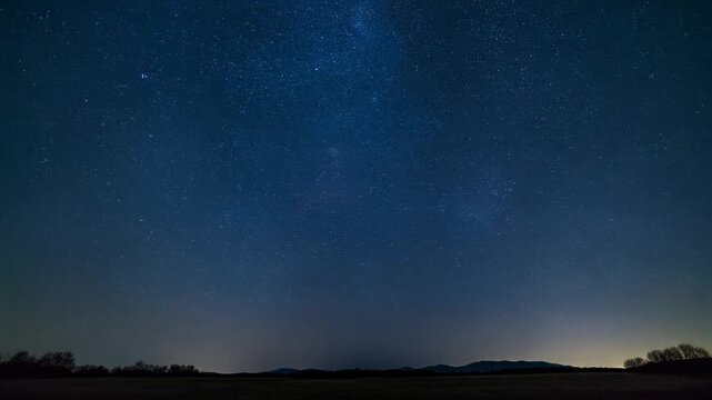 Timelapse of a starry night sky with a dark horizon silhouette