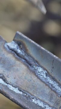 Slag removal techniques involve a metal chisel clearing residual waste from a steel weld joint in a workshop. Extreme close-up vertical shot.