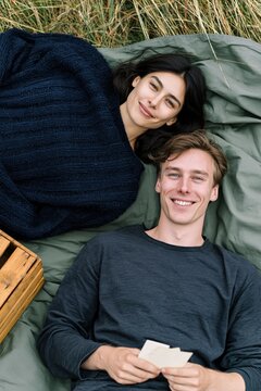 Smiling couple lying on a blanket outdoors holding photos for lifestyle picnic scene and romantic memory background