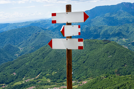 Wooden hiking signpost with three blank white and red directional arrows mockups on Monte Novegno mountain summit. Scenic alpine landscape on the background in Schio, Vicenza, Italy